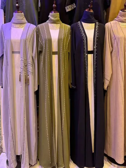 A collection of open front abayas in neutral tones like beige, olive green, and navy. These versatile pieces can be layered easily and feature subtle vertical beading and tassel details.