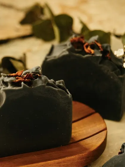 The 'Barood' charcoal body bar, shown here on a simple wooden dish. The rugged, natural top is formed as the soap sets, a signature of its handmade origin.