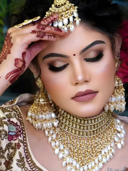 A close up of a bride wearing a stunning gold-plated kundan choker set, heavily embellished with pearls. This Punjabi-inspired bridal set includes a matching maang tikka and oversized jhumkas for a complete and elegant look.