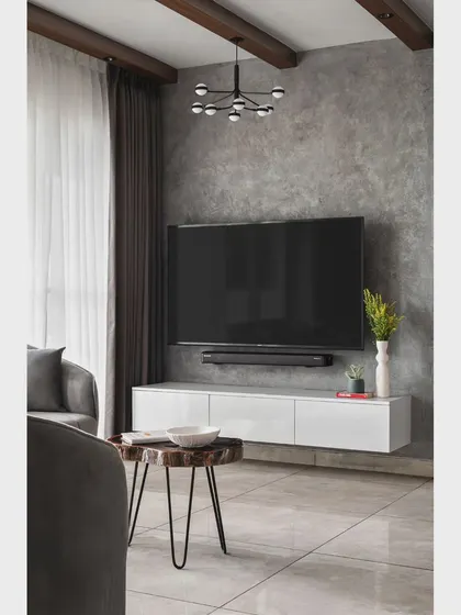 The media wall in the 'Nordic Grey Apartment' has a concrete texture, providing a raw, industrial contrast to the sleek white floating console. The modern chandelier adds a sculptural element.