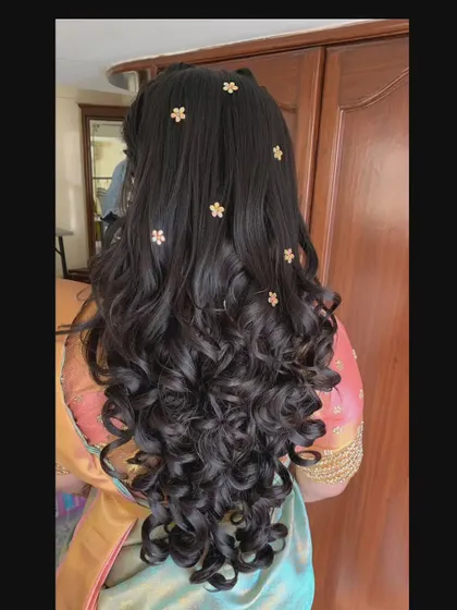 Long, cascading curls decorated with small, flower-shaped pins for a whimsical and pretty look.