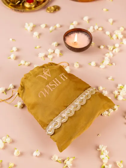 A mustard yellow "Thamboolam Tales" potli, surrounded by jasmine flowers and a lit coconut candle. This shot captures the modern yet traditional aesthetic of our wedding favors.