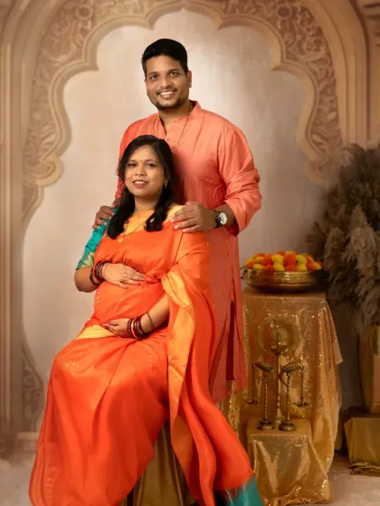 A formal portrait of the couple in their beautiful traditional attire. The husband stands protectively behind his seated wife, creating a classic and elegant composition.