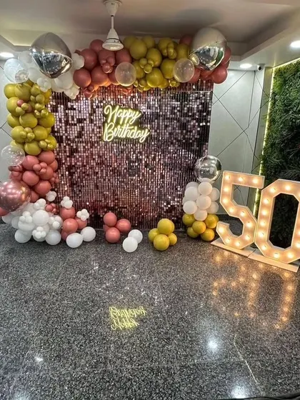 A grand 50th birthday celebration with a rose gold sequin wall, a colorful balloon arch, and large '50' marquee numbers.