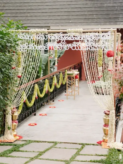 The entrance to the 'Pastel Panchangam' wedding, where guests are welcomed by an arch of cascading jasmine garlands. The design uses traditional brass pots and floral arrangements to set a sacred and inviting tone.