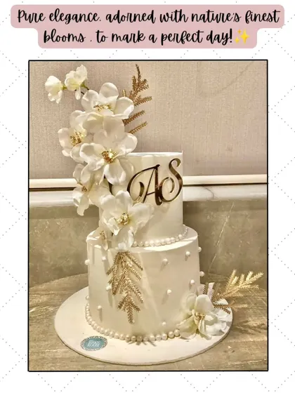 Pure elegance in white and gold. This two-tier cake is adorned with a cascade of handcrafted white sugar flowers and delicate golden leaves, perfect for an anniversary or intimate wedding.