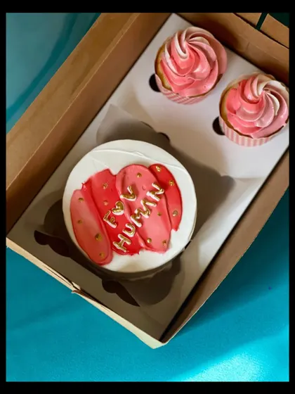 This elegant bento and cupcake box features a modern design with pink and red brushstrokes on the cake, highlighted with gold leaf. The two accompanying cupcakes have beautiful two-toned pink frosting swirls.
