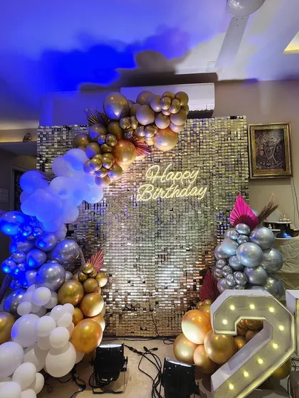Another angle of the 25th birthday shimmer wall setup. The blue uplighting adds a cool contrast to the warm gold tones of the balloons and backdrop, showing how lighting can change the mood.