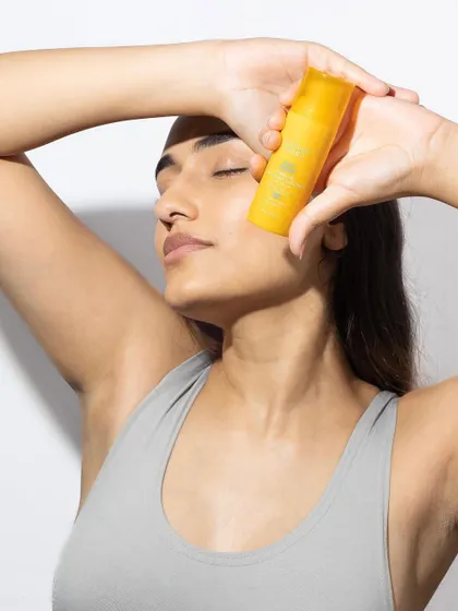 A serene and aspirational lifestyle shot. The model's relaxed pose and the way she holds the product to her skin convey a sense of calm and self-care.