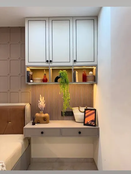 A compact study nook designed within a bedroom. It features a floating desk, drawers, and overhead cabinets, with fluted paneling and backlighting to create a warm, functional workspace.