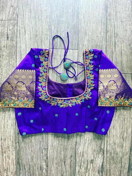A purple silk blouse with a gold and blue floral vine embroidered along the neckline. The sleeves feature a traditional brocade border.