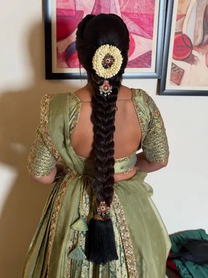 A classic fishtail braid adorned with a traditional floral and jewel piece. The black tassel at the end is a quintessential part of South Indian bridal hairstyles.
