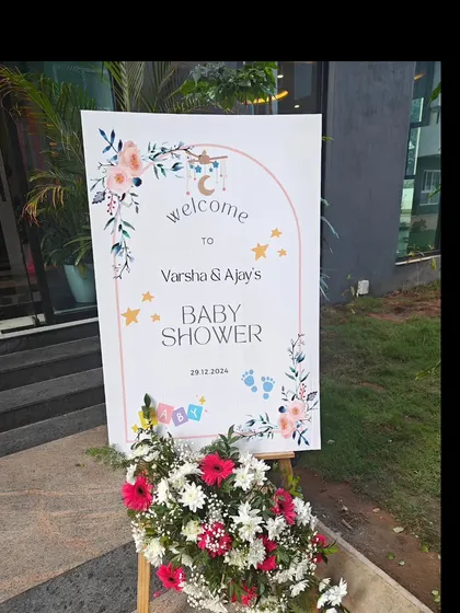 A simple yet elegant welcome sign for Varsha and Ajay's baby shower. The floral and celestial design, combined with fresh flowers at the base, creates a warm and inviting entrance for guests.