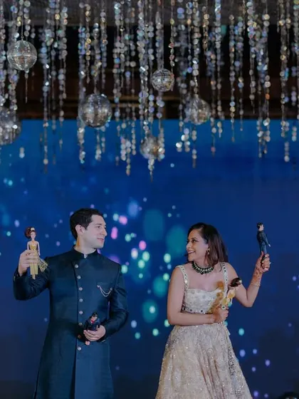A fun moment on stage during the Sangeet, with the couple holding up Barbie and Ken dolls, adding a playful and personal touch to their celebration.