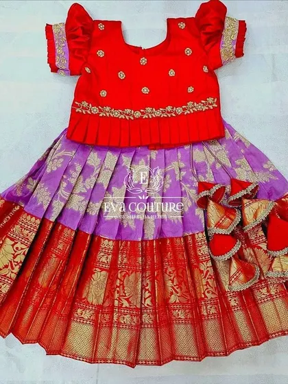 A newborn pattu lehenga in a classic red and purple combination. The red blouse has delicate embroidery, and the skirt has fun, oversized tassels.