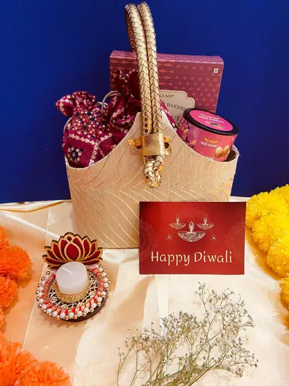 A beautiful beige basket with ornate golden handles, filled with sweets and a decorative lotus candle. This hamper is a blend of traditional and contemporary design.