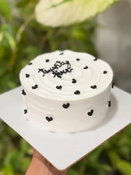 Minimal, chic, and effortlessly aesthetic. This monochrome cake features a clean white buttercream base with a swirl top and is dotted with tiny, elegant black hearts.