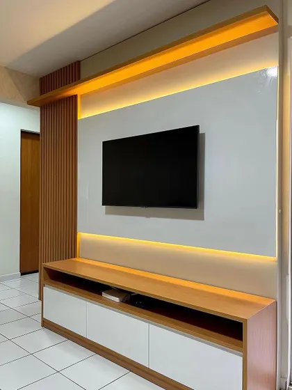 A beautiful and simple TV unit design with a wood and white laminate finish. The warm backlighting creates a cozy and inviting atmosphere.