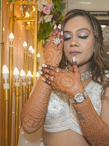 A portrait of a happy client at her engagement, showcasing her full-sleeve mehendi. The rich color and detailed patterns on her arms and hands complement her festive attire perfectly.