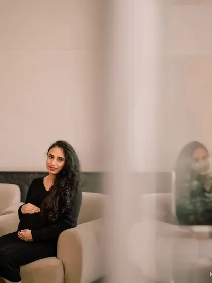 A solo portrait from the same indoor session. The artistic framing, shooting through a foreground element, adds depth and a sense of quiet intimacy to the photograph.
