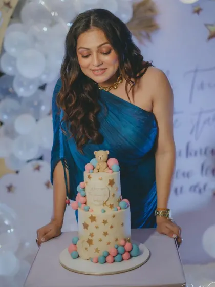 Actress Drashti Dhami admiring her "Twinkle Twinkle Little Star" themed baby shower cake. We designed this adorable two-tier cake with a teddy bear topper and a cascade of pink and blue spheres.