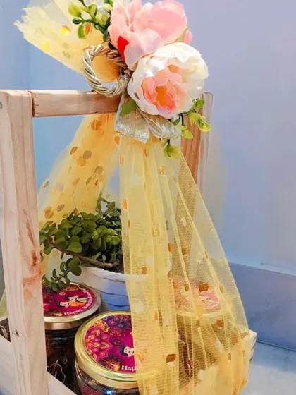 This wooden pinewood basket is a versatile and budget-friendly option for festivals like Rakhi. It can be filled with jars of dry fruits or chocolates and is beautifully decorated with yellow netting and flowers.