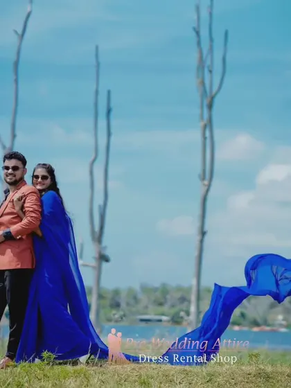 A wide shot of a couple by the lake, showing the full effect of the blue trail saree's long, flowing pallu against the open landscape.
