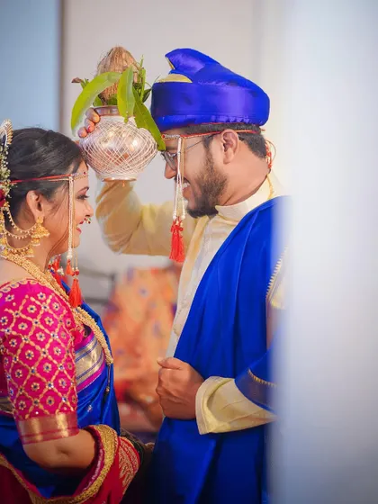 A beautiful moment from a Maharashtrian wedding vidhi. The groom holds a sacred kalash over the bride's head, and their shared smile captures the happiness of the ritual.