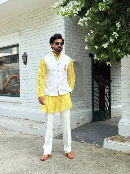 Make a vibrant statement at your next Haldi or Sangeet ceremony. This bright yellow patterned kurta is layered with a crisp white Nehru jacket, creating a look that is both festive and dapper.