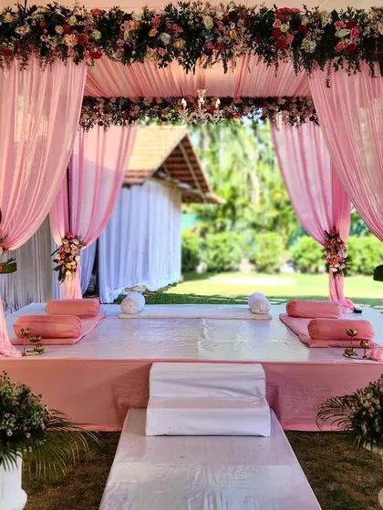 This elegant pink mandap was designed for an outdoor engagement. The soft drapes are complemented by a thick border of multi-colored premium flowers, with a chandelier adding a touch of glamour.