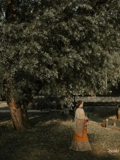 A serene portrait of the bride under a large willow tree in Kashmir, a moment of quiet beauty before the festivities.