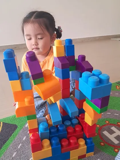 A towering, colorful structure made from large plastic blocks showcases this child's creativity and understanding of balance.