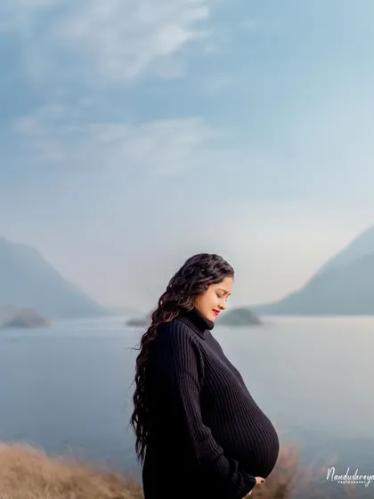 A solo portrait capturing a moment of quiet reflection by the water. The vastness of the landscape highlights the personal and profound journey of motherhood.