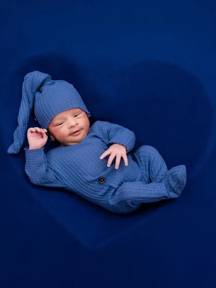 A newborn boy in a blue outfit rests inside a heart-shaped prop, looking calm and content. A simple yet powerful image.