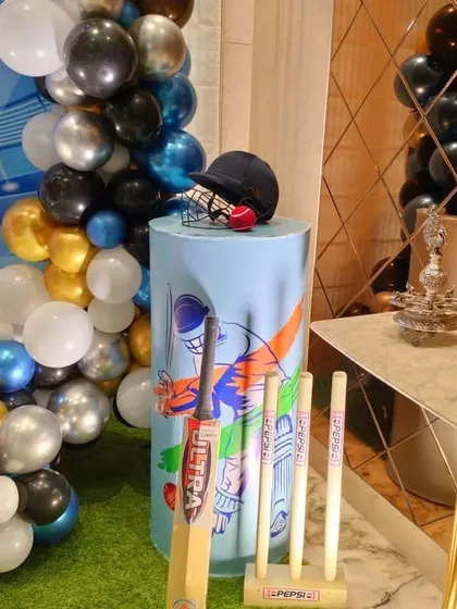A close-up of a pedestal decorated with cricket equipment props like a bat, ball, and helmet.
