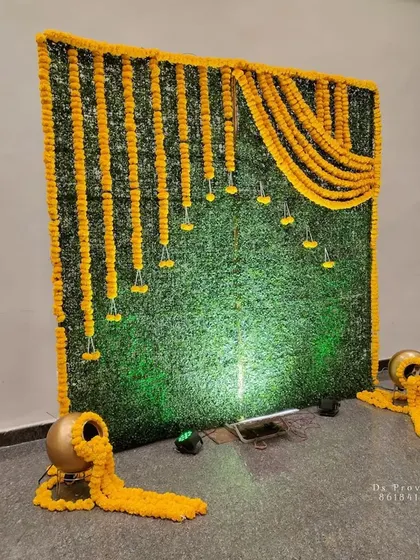A classic backdrop design using an artificial green grass mat. I've decorated it with hanging marigold strings and small floral bunches, with traditional brass pots at the base.
