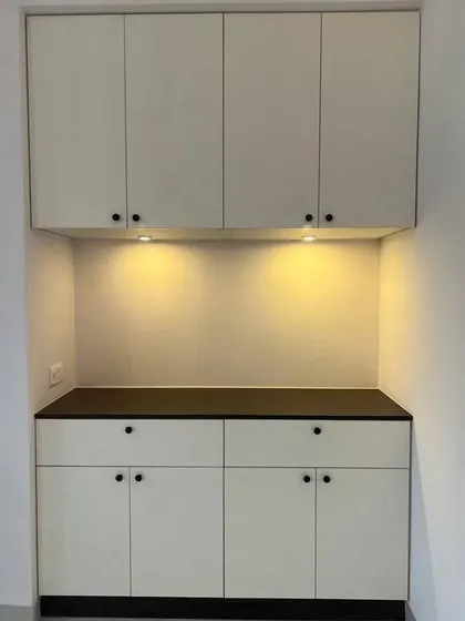 A simple and elegant crockery or storage unit in off-white with minimalist black knobs. The under-cabinet lighting provides useful task lighting for the countertop.