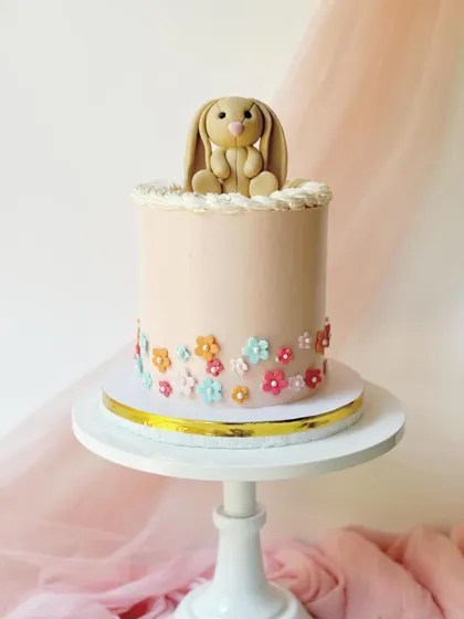 A simple and elegant bunny cake. A single fondant bunny sits on top of a smooth pink buttercream cake decorated with a border of tiny flowers.
