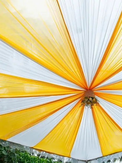 The canopy for a Haldi ceremony, featuring radiating drapes of yellow and white fabric. This simple yet effective decor element provides shade and adds to the festive look of the outdoor event.
