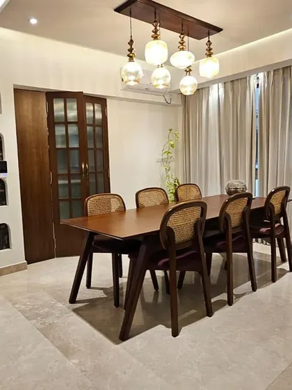 For those who believe dinner tastes better under a chandelier, with chairs that match the conversation. An elegant dining setup with a wooden table and cane-back chairs.