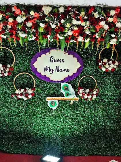 A closer view of the green wall backdrop, highlighting the floral details in hanging rings and the Krishna-themed elements for a naming ceremony.