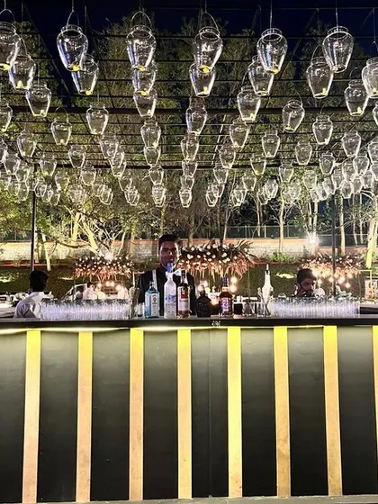 A stunning bar setup for a grand event, featuring a black and gold striped counter under an elaborate canopy of hanging glass lanterns. This design creates a truly magical and upscale atmosphere.