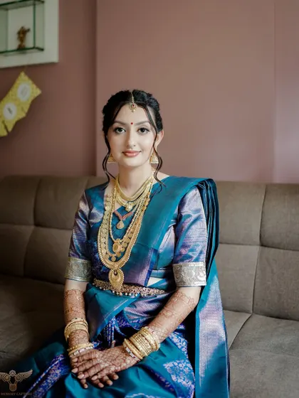 A seated portrait showing her full Pheras look. The makeup is designed to complement the rich colors of her saree and the heavy gold jewelry.
