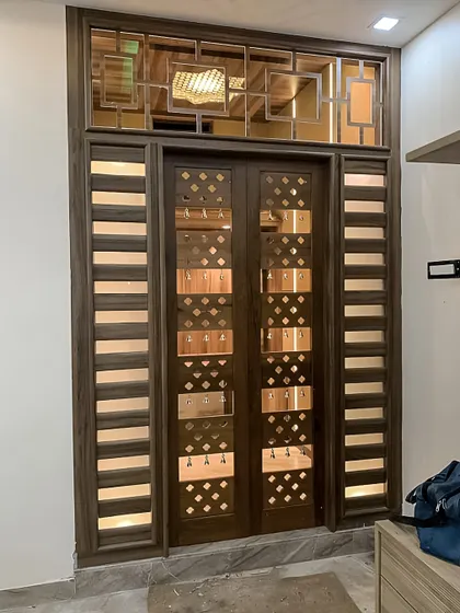 A custom-designed pooja room door made of wood with intricate metal and glass detailing. The design allows light to filter through while creating a grand and sacred entrance.
