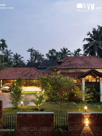 A dusk view of Kuttiyil House, showcasing the classic Kerala architectural style with its prominent sloped roofs and welcoming porch, surrounded by lush greenery.