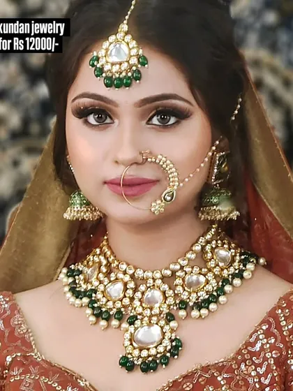 A beautiful Kundan jewellery set with a large maang tikka and jhumkas, featuring green and white stones. This complete set is available for purchase.