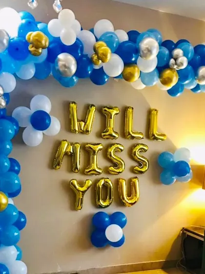 A "Will Miss You" farewell party decoration. This home setup features a blue, white, and gold balloon arch with foil letters.