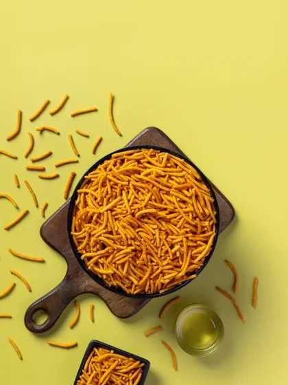 A top-down shot of spicy sev on a yellow background. The composition leaves ample copy space, making it a versatile asset for packaging and advertising.