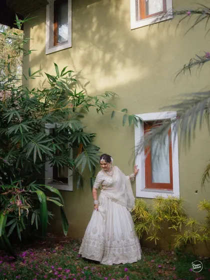 A full-length portrait of the bride against a charming, rustic wall, showcasing her elegant white lehenga.
