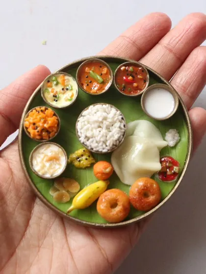 A complete South Indian thali held in the palm, showing the intricate arrangement of over 15 tiny items.